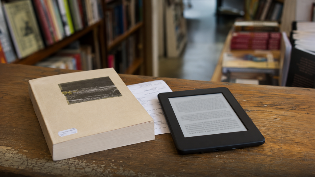 POR QUÉ UN LIBRO DE KINDLE PUEDE COSTAR MÁS QUE LA EDICIÓN EN PAPEL Un lector electrónico junto a un libro impreso sobre el mostrador de una librería.